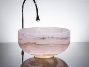 Modern bathroom sink with a polished metal faucet and round marble basin on reflective surface.