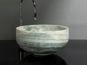 Modern round stone sink with green and white marble patterns paired with a sleek tall chrome faucet.