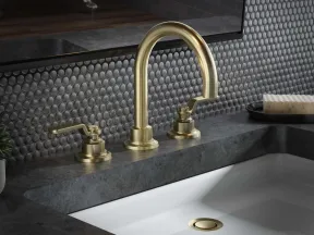 Modern bathroom sink with brushed gold faucet and gray penny tile backsplash under a mirror