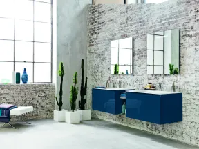 Modern bathroom with blue floating vanity cabinets, white brick walls, tall cacti, and large industrial-style windows.