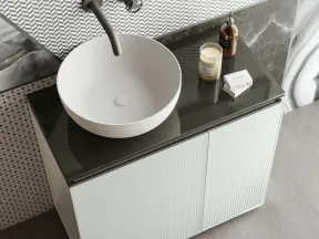 Modern white bathroom sink with round basin, black countertop, patterned wall, and vanity cabinet below.