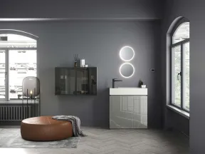 Modern bathroom with round illuminated mirrors, gray vanity, leather ottoman, and large arched windows with city view.