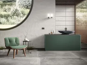Modern bathroom interior with green vanity, round window overlooking garden, green chair, and gray floor tiles