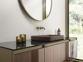Modern bathroom vanity with a round mirror, matte black countertop, mauve sink, and glass cabinet doors by a large window.