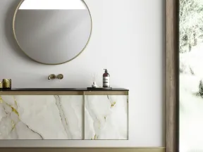 Modern bathroom vanity with marble cabinet, round mirror, gold faucet, and large window with natural light.