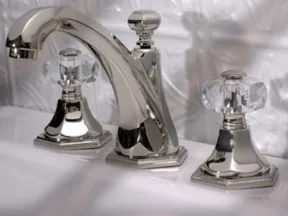 Polished chrome bathroom faucet with crystal clear dual handles on a white sink with embossed tile backsplash.