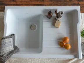 White kitchen sink with oranges, soap bottle, cleaning brush, and folded towels on wooden table.