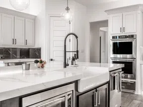 Bright modern kitchen with marble countertops, white cabinets, stainless steel appliances, and a black faucet.