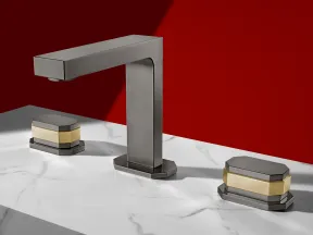 Modern metallic faucet and dual handles with gold accents on white marble countertop against red wall.