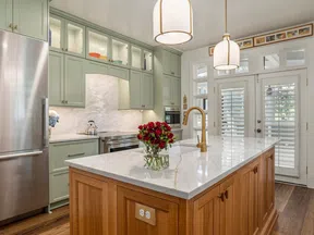 Modern kitchen with light green cabinets, stainless steel refrigerator, wooden island with marble countertop and pendant lights.