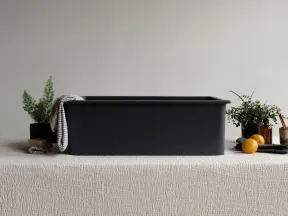 Black rectangular storage bin on textured cream tablecloth with plants, oranges, and bathroom items around it