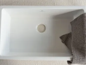 Empty rectangular white ceramic sink with central drain hole and gray textured towel on the right side.