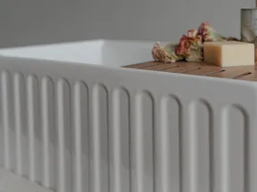 Modern white ceramic sink with ribbed sides featuring a wooden tray holding soap and dried flowers.