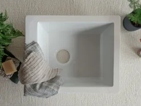 Top view of a clean white rectangular sink with a hole for drainage surrounded by plants and towels.