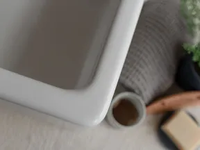 Close-up of a white ceramic sink corner with bath accessories and towel in soft focus.