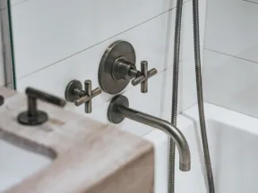 Matte black wall-mounted faucet and handles over a white bathtub with tile backsplash and stone countertop.