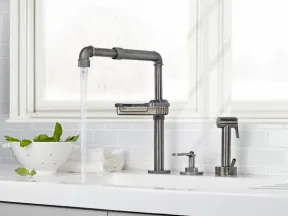 Modern industrial-style kitchen faucet with running water, soap dispenser, and vegetable sprayer on white countertop.