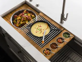 Kitchen sink setup with queso dip, multicolored chips, and four small bowls of different sauces on a wooden tray.