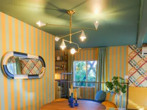 Cozy dining area with round wooden table, mustard yellow chairs, striped walls, and modern chandelier.