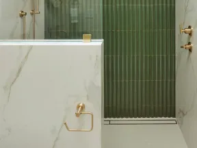 Modern bathroom shower with green ribbed tiles, gold fixtures, glass partition, and marble walls under recessed lighting