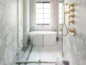 Luxurious bathroom with marble walls, gold fixtures, freestanding tub, and glass-enclosed shower with patterned floor tiles.