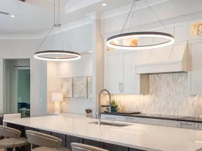 Modern kitchen with a large white island, beige bar stools, circular pendant lights, and white cabinetry.