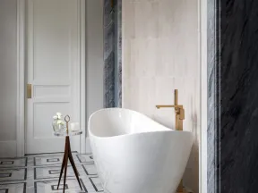 Modern white freestanding bathtub with gold faucet, geometric tiled floor, and minimalist decor in luxury bathroom.
