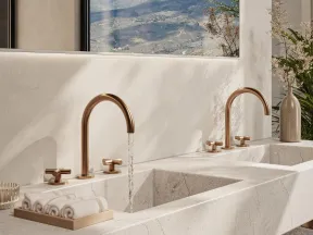 Modern double marble sink with gold faucets, decorative towels, and plants in a bright bathroom setting.