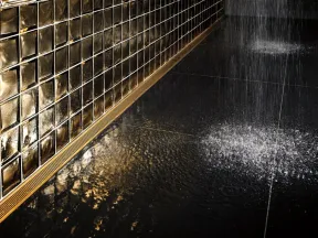Modern shower with rain water flow, reflective black floor, and stylish golden mosaic tiled wall
