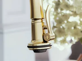 Close-up of a modern gold kitchen faucet with lever handle against blurred white flowers background