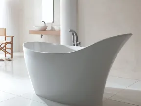 Modern freestanding white bathtub in a minimalist bathroom with white walls and wooden chair.