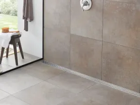 Modern bathroom shower area with large grey tiles, a wooden stool, plants, and a glass partition.