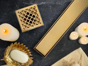Luxurious gold bathroom accessories with white candles, soap on a leaf dish, sponge, and folded towels on black marble.