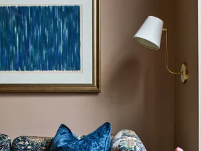 Cozy corner with floral patterned sofa, plush blue pillow, marble side table with vase, and modern wall lamp.