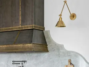 Modern kitchen with brass range hood, marble backsplash, gas stove with red knobs, and wooden utensils.