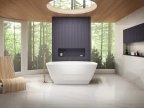 Modern bathroom with a white freestanding tub, wooden chair, skylight, and forest view through large windows.