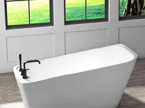 Modern white freestanding bathtub with black faucet near large windows overlooking green lawn.