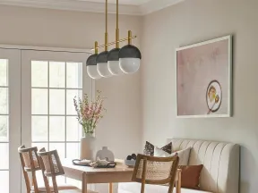 Modern dining room with wooden table, cane-back chairs, beige banquette seating, pendant lights, and floral centerpiece.