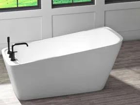 Modern white freestanding bathtub with black faucet in a bright room with wooden floor and large windows.