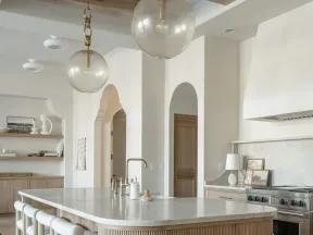 Modern kitchen with wooden island, marble countertop, pendant lights, and light wood cabinetry in neutral tones.
