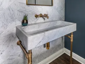 Modern bathroom with marble sink, brass fixtures, chevron marble wall tiles, and a blue accent wall.