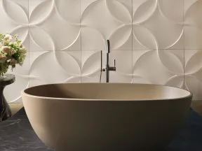 Modern beige freestanding bathtub with geometric 3D wall tiles and floral arrangement on side table.