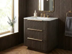 Modern bathroom vanity with ribbed dark wood cabinetry, brass hardware, white countertop, mirror, and natural light window.