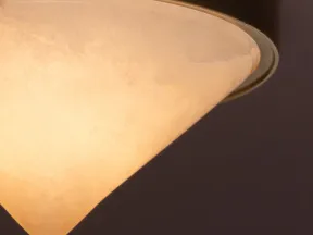 Close-up of a warm glowing conical ceiling light fixture with brass trim against a dark background.