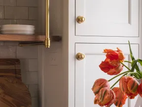 Modern kitchen corner with white cabinets, dark countertops, brass handles, wooden cutting boards, and orange tulips.