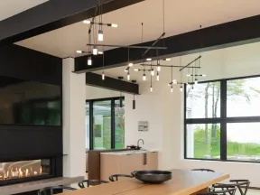 Modern dining room with wooden table, black chairs, large windows, and contemporary pendant lighting above.
