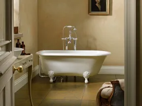 Vintage clawfoot bathtub with silver faucet in classic beige bathroom featuring a portrait and antique furniture.