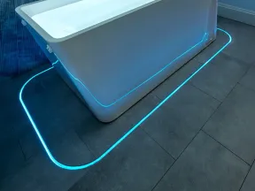 Modern white bathtub with blue LED lighting on gray tiled floor and marble wall background in bathroom