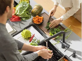 Couple washing and chopping fresh vegetables in a modern kitchen with various produce on the counter