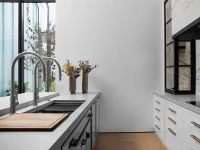 Modern kitchen with white cabinets, marble backsplash, wooden floor, dual sinks, and sleek stainless faucets.